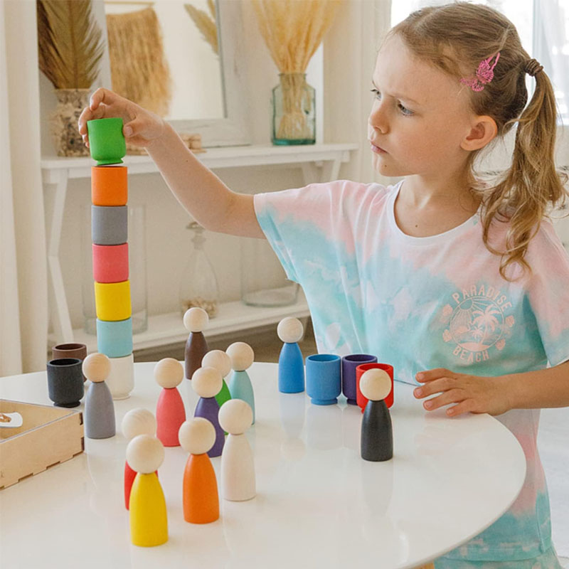 A collection of minimalist Waldorf wooden toys, including a rainbow stacker and faceless peg dolls.