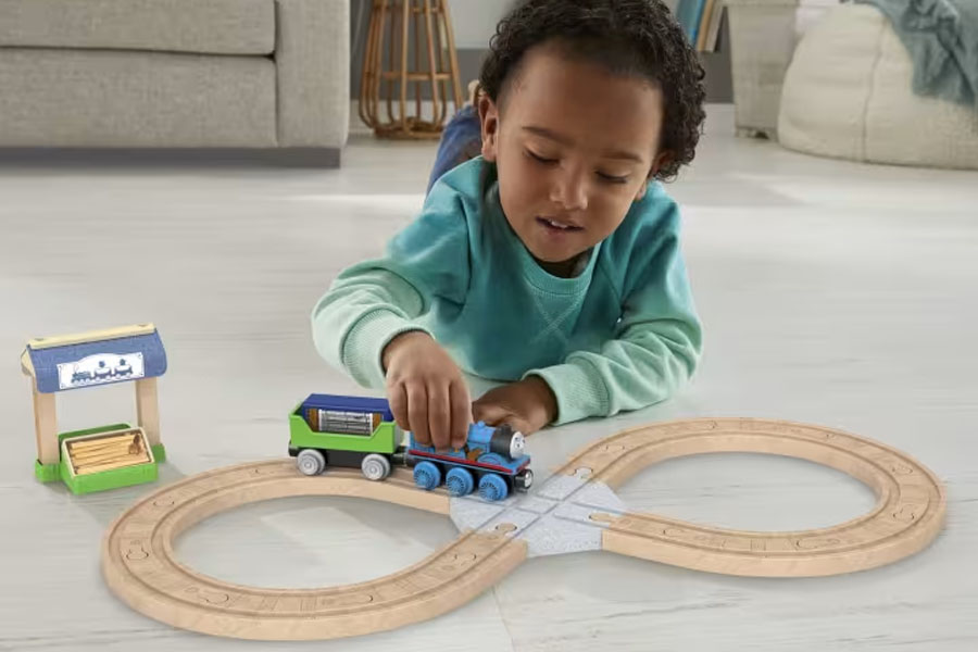 A child building an elaborate wooden train track layout on the floor of their room.