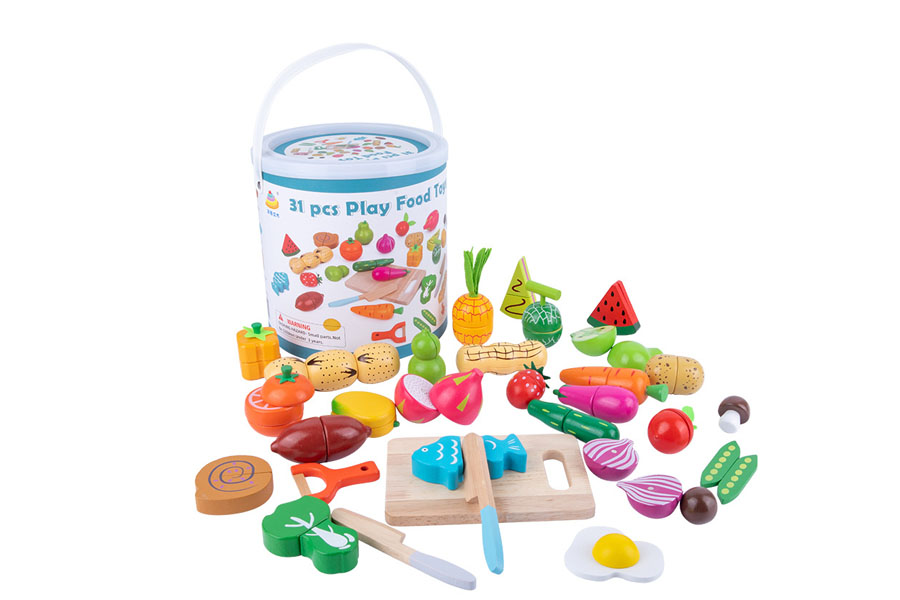 A child happily placing a wooden broccoli floret and a slice of tomato on a play plate