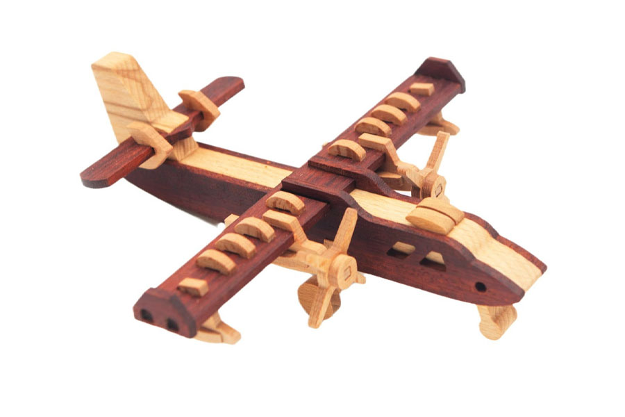 A child running through a grassy field, holding a wooden plane high in the air as if it's flying.