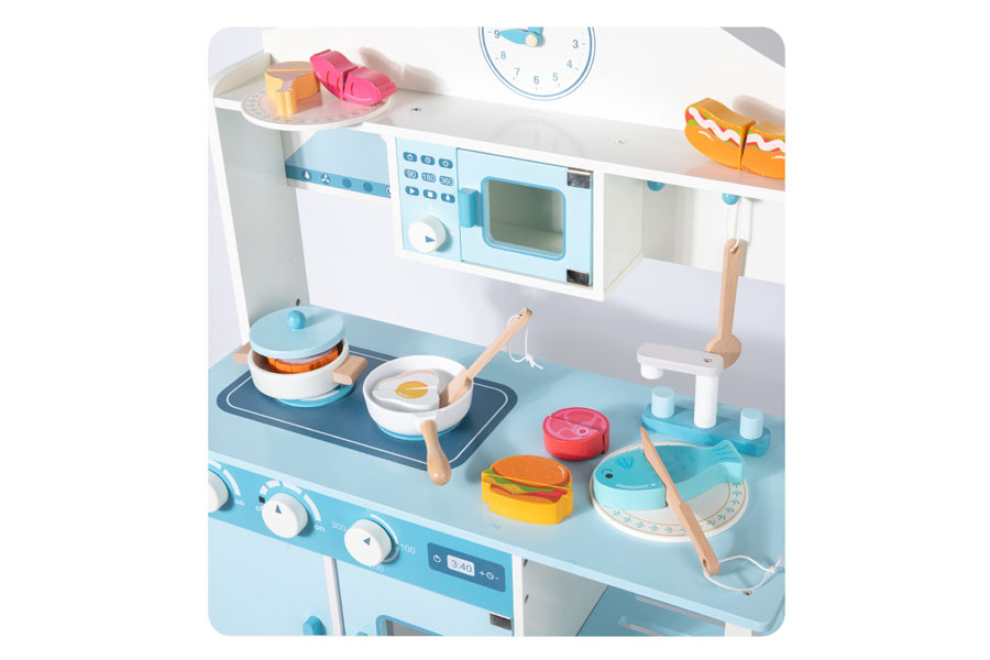 A smiling toddler carefully  washing a wooden plate in the sink of their toy kitchen.