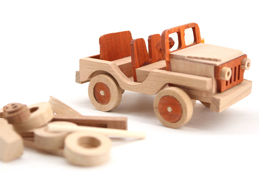 A toddler's hands pushing a chunky wooden truck across a wooden floor.