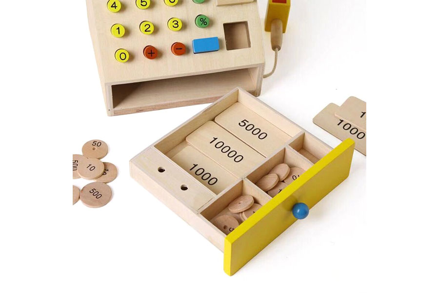 A wooden cash register on a simple shelf in a calm, organized Montessori-style classroom