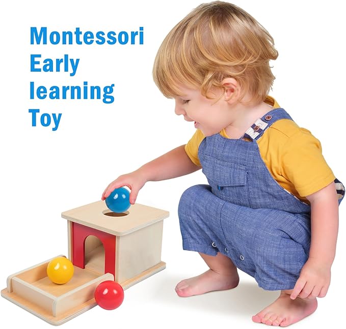 A one-year-old intently dropping a wooden ball into a Montessori object permanence box